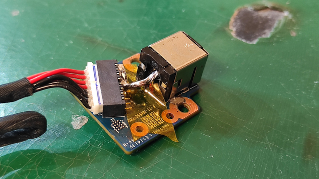 A close-up view of a small circuit board with a repaired laptop power module. The wires are neatly soldered, and Kapton tape is used for insulation.