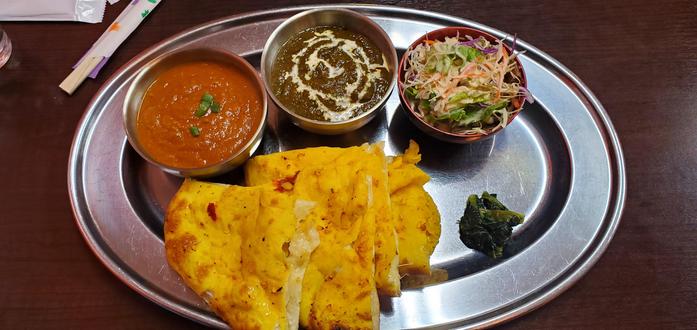 A garlic cheese naan with two types of Nepali curry and a peanut dressing salad all on a silver tray from the restaurant Surya in Japan.