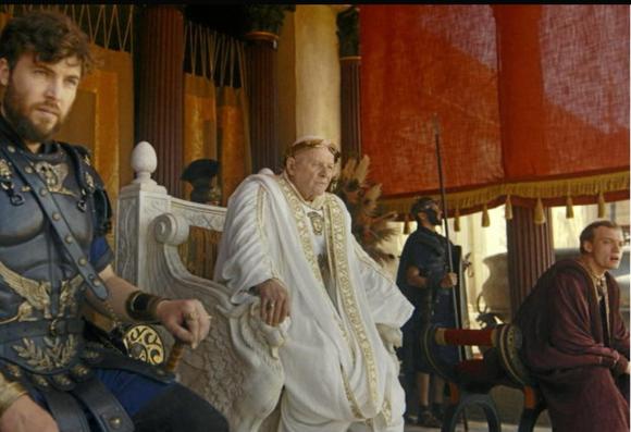 El palco del Circo Máximo, con el emperador Vespasiano (Anthony Hopkins) ricamente ataviado y con la corona de laurel de oro sentado en el trono de mármol flanqueado por sus dos hijos.