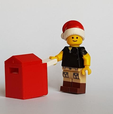 Photo is Lego Pete Carrier wearing a Santa hat posting a thin package into a red post box.