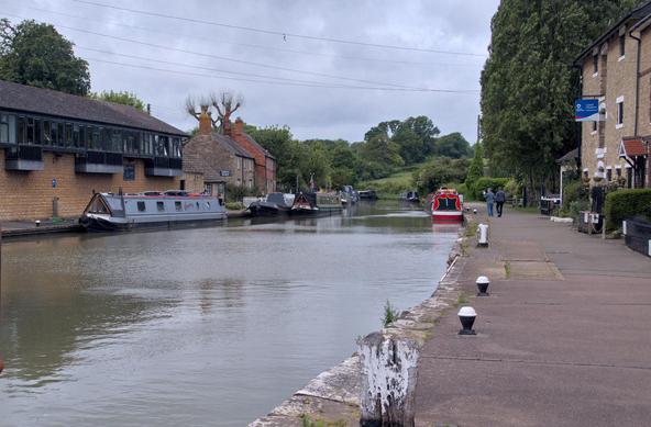 A wide stretch of the Grand Union canal at Stoke Bruerne. Overcast sky. Several narrowboats can be seen, some preparing to descend the (unseen) flight of locks to the southeast (behind the camera).