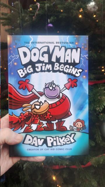 A copy of Dog Man - Big Jim Begins being held up next to the Edinburgh Bookshop Christmas tree