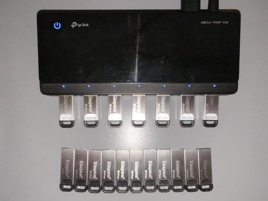 Ein schwarzer USB-3-Hub mit sieben eingesteckten metallisch glänzenden USB-Sticks. Davor liegen elf weitere USB-Sticks, die darauf warten, bespielt zu werden.

Foto: CC by @chpietsch@fedifreu.de