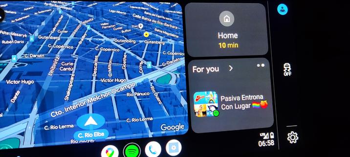 Fotografía de una pantalla de Android Auto mostrando un mapa y una recomendación de Spotify para una lista de reproducción con el título "Pasiva, entro a y con lugar" acompañada de emoticones de bandera LGBT y un durazno.