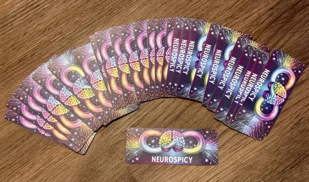 Stickers that say Neurospicy. The background is a rainbow colored image with a brain in the middle and an infinity loop behind it.