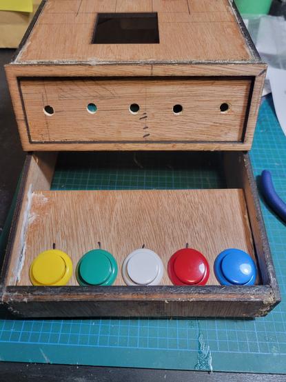 An open bottom housing case made of wood, a platform inside, glued in place holds 5 arcade buttons.