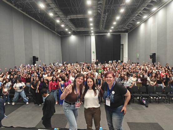 Delante de un auditorio repleto, las escritoras Joana Marcús, Alice Kellen y Raquel Castro posan, sonrientes.