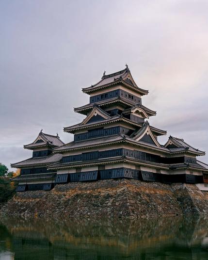 A Japanese castle with a green pond at the bottom of the frame.