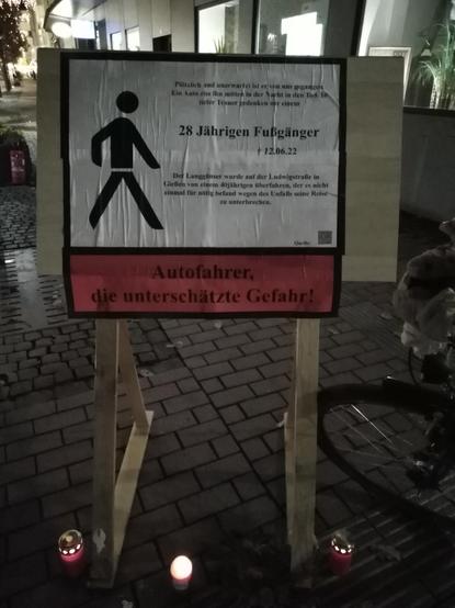 Ein Standschild steht in der Fußgängyzone in Form einer Traueranzeige. Unterhalb des Schildes stehen Grabkerzen. Auf dem Schild ist linksbündig ein Fußgängysymbol abgebildet. Rechtsbündig stehen folgende Zeilen in unterschiedlicher Schriftgröße:
"Plötzlich und unerwartet ist er von uns gegangen. Ein Auto riss ihn mitten in der Nacht in den Tod. In tiefer Trauer gedenken wir einem 

[hervorgehoben]  28 Jährigen Fußgänger
[Kreuzsymbol] 12.6.22

Der Langgönser wurde auf der Ludwigstr. in Gießen von einem 40jährigen überfahren, der es nicht einmal für nötig befand wegen des Unfalls seine Reise zu unterbrechen."
Unterhalb ist rot unterlegt im Stil einer Zigarettenschachtelwarnung der Text angebracht: "Autofahrer, die unterschätzte Gefahr!"