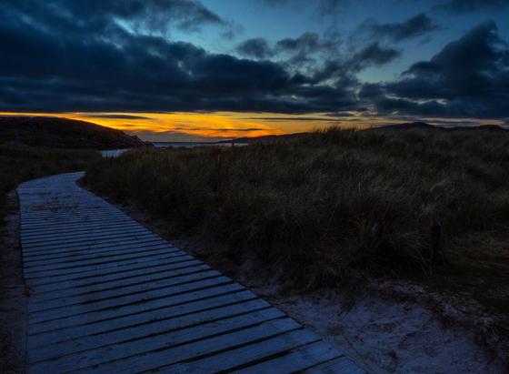 On Scotland's west coast North Coast 500 route, it's a perfect location for an image of a remote beach just after sunset, the timber board walk through the grasses, leads the way to the distant gold sunset horizon for a spot of night swimming perhaps.