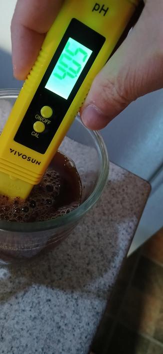 A Vivosun pH meter reading 4.05 pH, being held by hand in a glass mug filled with a darkish brown liquid.