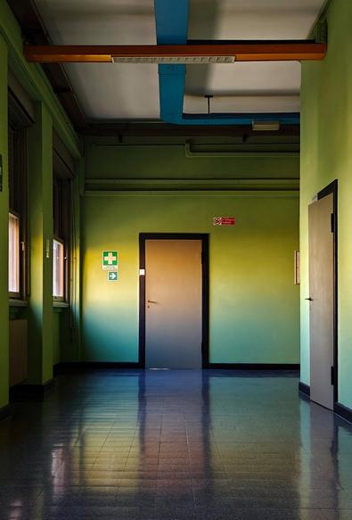 A corner of a corridor, with a polished reflecting floor and green walls, brown doors and  blue and copper cable trays at the ceiling.