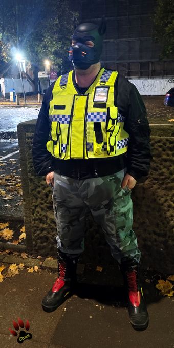 human pup, wearing camo trousers, haix boots and a hi-vis vest standing on the boardwalk in Manchester at night, full view
