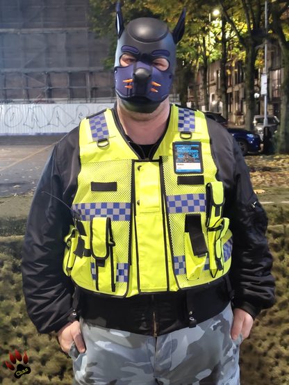 human pup, wearing camo trousers, haix boots and a hi-vis vest standing on the boardwalk in Manchester at night, bust shot