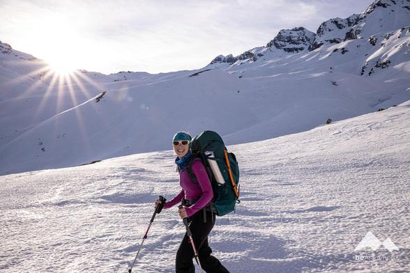 woman on a ski tour smiling, sun in the background, snow everywhere.