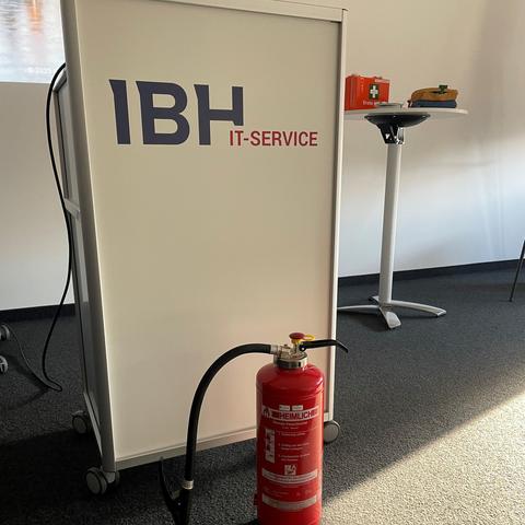 Feuerlöscher im Vordergrund und ein Sprechpult der IBH im Hintergrund im großen Meetingraum der IBH IT-Service