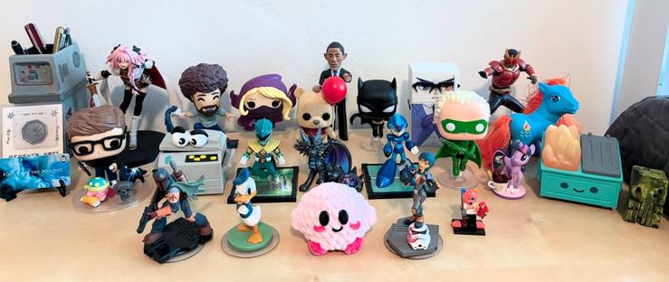 Figures arranged on a desk, from back-left to front-right: Gonk Droid, Astolfo, Bob Ross, Batgirl, Winnie the Pooh, Barack Obama, Batgirl, Refrigerator-senpai, Kamen Rider Kuuga, Memento Mori coin, Focus on the Positive, James Huff, sleeping Kirby, dog, wolf, Coppy, Green Ranger, dragon, Mega Man X, Green Lantern, Twilight Sparkle, Waterfire, Dumpster Fire, Cthulhu, Boba Fett, Donald Duck, yarn Kirby, Sabine Wren, and Cuddly Captain.