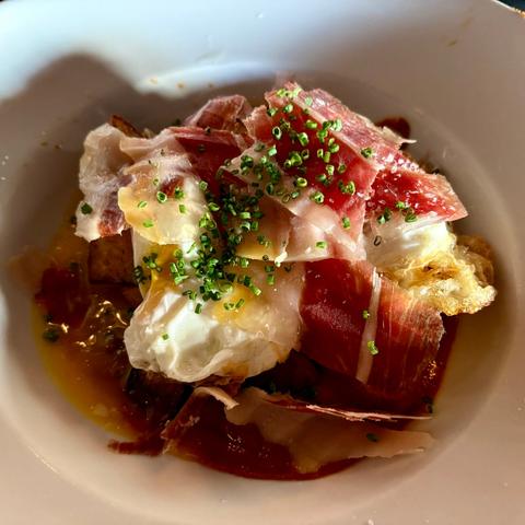 A bowl of potatoes, fried eggs, and Iberico ham, on a delicious brava sauce.