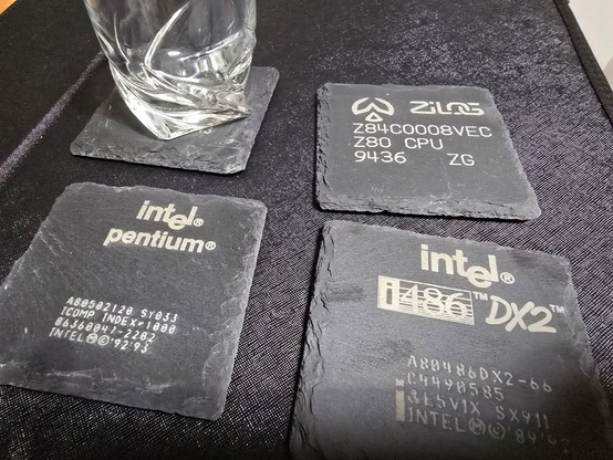Laser engraved slate coasters showing markings of a z80, a pentium, a 486 and a 68k with a glass on it.
