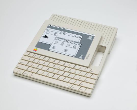The actual 1984 Apple Macintosh touchscreen tablet prototype. This device is flat with a display and a keyboard underneath it. It has an integrated handle on the right side. There’s no bezel around the keyboard, and each key is shaped like a trapezoid.