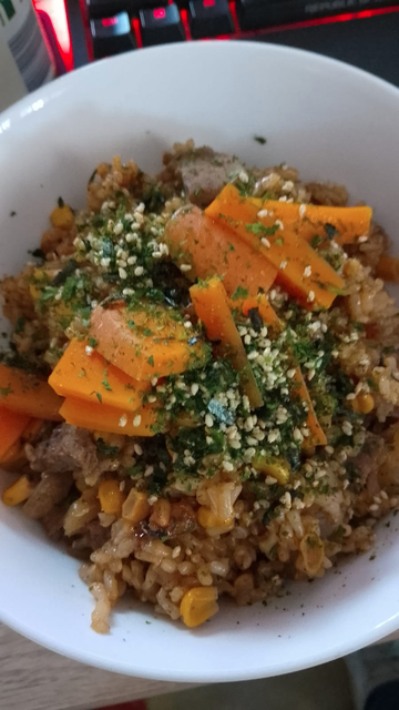 A white bowl holding brown rice, onion, corn, carrots and beef with some furikake on top.