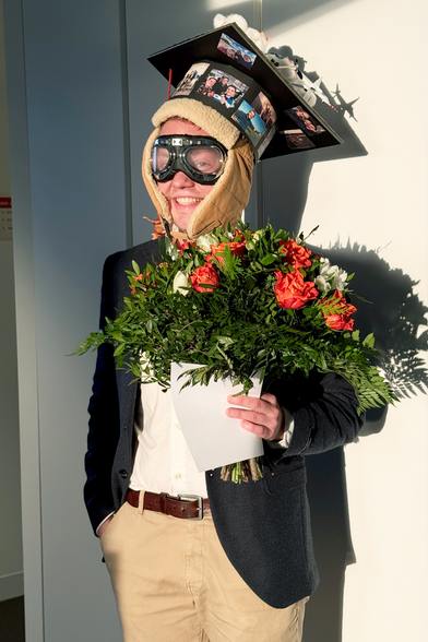 Henning Dorff wearing goggles and a PhD hat and holding a bouquet of red and white roses.