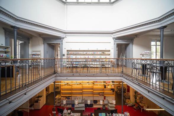 An octagonal atrium surrounded by a mezzanine resting on cast iron pillars. There are bookshelves against the walls and a book sorting area on the lower floor.