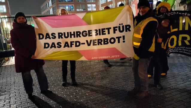 Menschen mit Banner vor einem erleuchteten Bürogebäude. Das Banner: "Das Ruhrgebiet für das AFD-Verbot"
