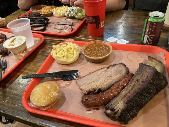 Several trays of barbecued meat with sides like mac & cheese, baked beans, and cornbread.