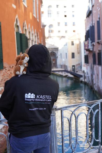 Flag-squirrel sitting on the left shoulder of a person looking at a lagoon in Venice.