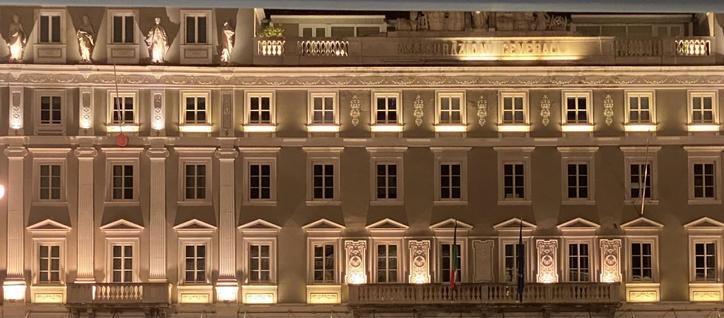 Palazzo Stratti an der Piazza Unità d‘Italia, Triest. Die beleuchtete Fensterfront bei Nacht.