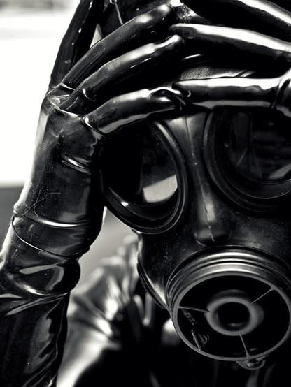 A close up photo of a person wearing a gas mask with their hands held to their forehead