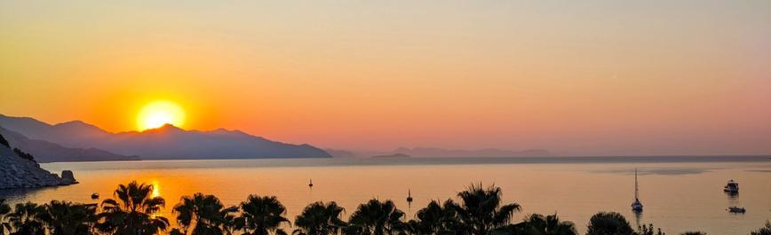 Sunrise. Mountain on the left. Sea in front. Some boats.

Sonnenaufgang. Links der Berg. Vorne das Meer. Einige Boote.