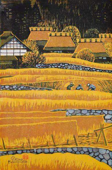 Rice is harvested on a farm in rural Japan. A series of terraced rice fields dominate the image, traveling from the foreground to the background like rolling waves. In the foreground, golden sheaves of rice have been hung up to dry on wooden racks, while figures continue the harvest on terraces further on. At the far end of the image, thatched-roof farmhouses stand close together, tucked in beneath tall dark trees.