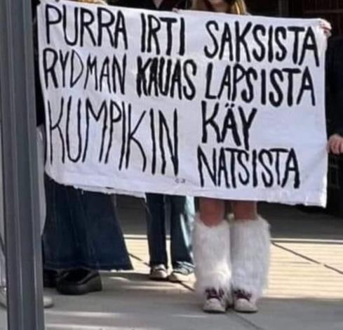 Kuvassa mielenosoitusbanderollin asiallinen tiivistys: "Purra irti saksista, Rydman kauas lapsista, kumpikin käy natsista."