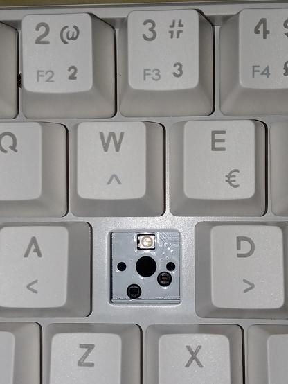 Foto mostrando a região das letras W A S D do teclado KBM! TG600, sem a keycap e sem o switch, é possível ver a placa de circuito, que tem a cor branca com "verniz".