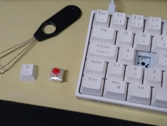 Foto do teclado KBM! TG600 sobre a mesa, sem a keycap e switch, que estão ao lado esquerdo dele