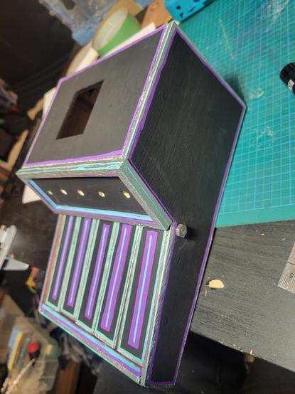 Side profile with top. A homemade keyboard /organ painted black with silver trim, teal highlits on the corners and edges, and purple interior trim. The keys now have a teal line through a purple rectangle down the middle length of the keys