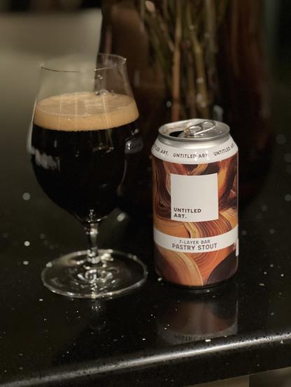 A snifter full of dark beer. The 12 ounce can is to the right, its label in splashes of shades of brown like chocolate and caramel. A white square holds the words “untitled art”
