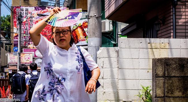 Dona que es protegeix amb un ventall del sol insofrible de l'estiu toquiota,