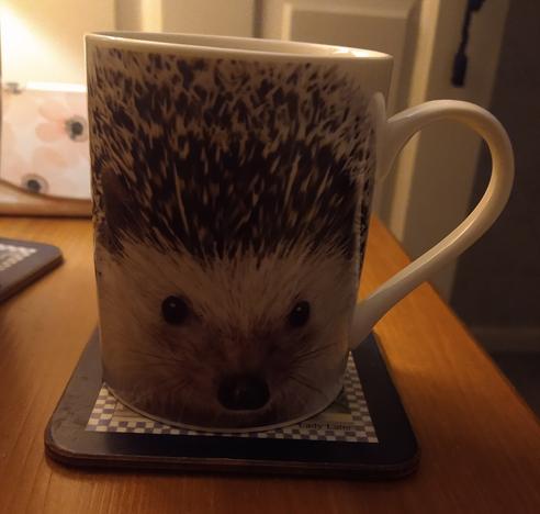 Mug of tea on a bedside cabinet with the face of a hedgehog
