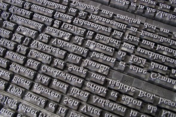 Nahaufnahme von Drucklettern in einem Setzkasten, die für den Buchdruck verwendet werden. Die Buchstaben sind spiegelverkehrt und aus Metall gefertigt.