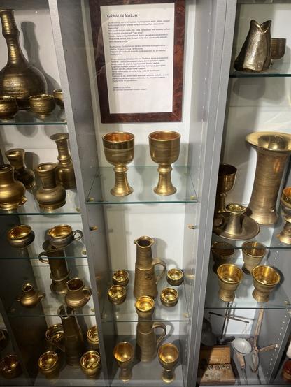 A display case containing various Savitorppa artifacts, including cups, goblets, pitchers, and other decorative items, with a placard discussing the significance of the Graal cup in Christian mythology.