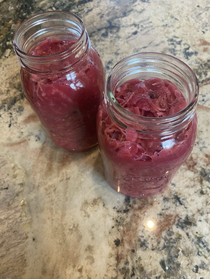 The photograph features two quarts of ferment. The open jars are viewed from three quarter above. The ferment is shredded red cabbage and leeks which float in the thick brine.