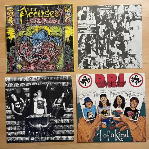 Zwei Schallplattenhüllen, jeweils daneben ist das Inlay. Links oben ist das Album „Martha Splatterhead's Maddest Stories Ever Told“ von der Band The Accüsed. Darauf abgebildet ist ein blaues Monster mit gelbem Irokesenschnitt, welches den Kopf eines anderen Monsters mit riesigen Zähnen entzweit. Daneben das Inlay mit verschiedenen schwarz-weiß Fotos.
Darunter ist das Album „4 of a Kind“ der Band D.R.I. Darauf ist eine Zeichnung, eine Hand hält vier Karten auf denen die Band Mitglieder sind. Auf jeder Karte steht Joker.