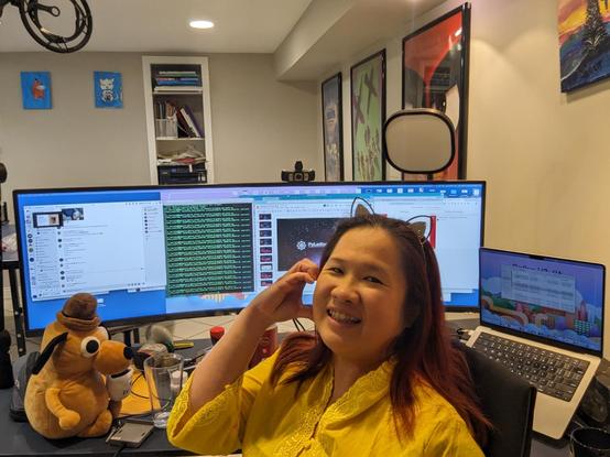 Mariatta seated in front of her desk and monitors, heart check pose