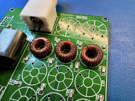 The green mcHF RF PCB. In the center there are three red ferrite toroids with copper enameled wire wound around them. From left to right they have 24, 27 and 24 windings each.