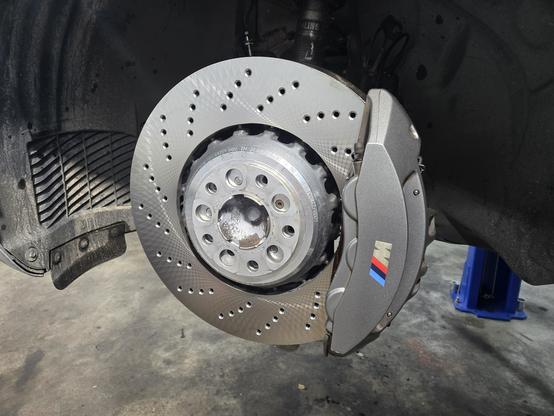 A large new brake rotor installed on a car with a silver caliper installed with the M logo in it.