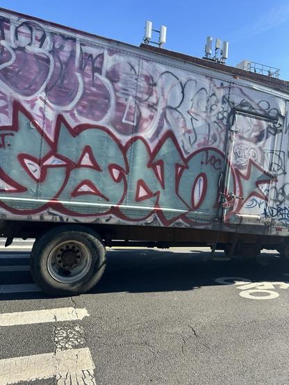 a white truck covered in graffiti, including CANO in teal arrow letters with a maroon outline
