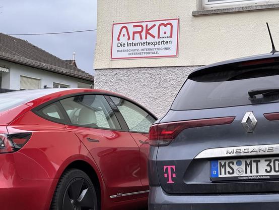 Blick auf das Bürogebäuse von ARKM - Die Internetexperten. Dafür steht ein roter Tesla Model 3 von ARKM und ein Firmenfahrzeug - Renault Megane in grau - der Deutschen Telekom.